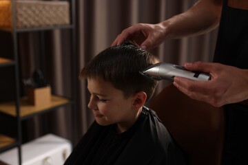 Professional barber working with little boy in barbershop, closeup