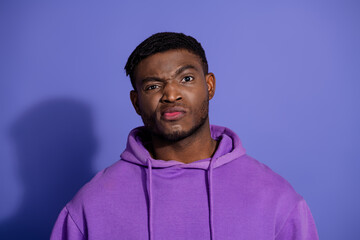 Fototapeta premium Young man wearing a purple hoodie posing against a vibrant background with a unique facial expression and styled look