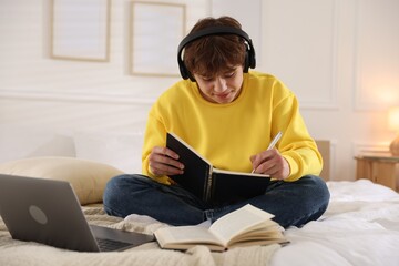 Teenage student in headphones studying on bed at home