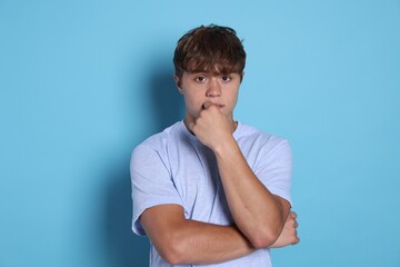 Teenage boy suffering from panic attack on light blue background