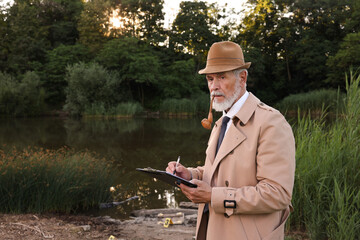 Forensic expertise. Detective with smoking pipe and clipboard working at crime scene near lake...