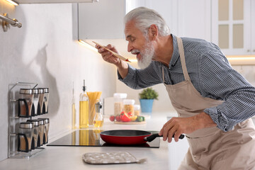 Elderly man cooking dish on cooktop in kitchen
