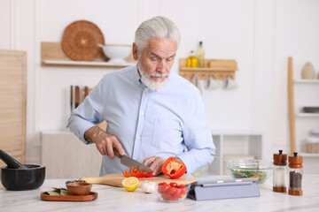 Elderly man cooking at white marble table in kitchen