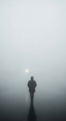 Fototapeta premium Solitary figure walking through dense fog on a quiet path with a distant light illuminating the scene