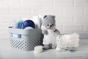 Many different baby accessories and toy bear on table near brick wall