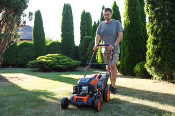 Man cutting green grass with lawn mower in garden