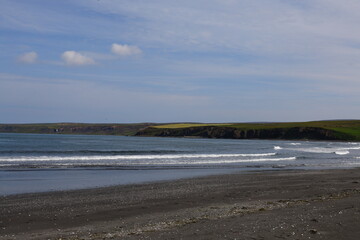 Rolling waves wash ashore a black sand beach on the northern Icelandic coast. The horizon is framed by distant cliffs, creating a natural and dramatic seascape full of raw beauty.