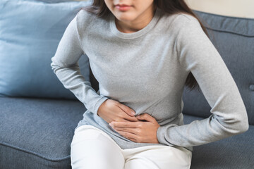 Fototapeta premium Sick asian young woman in pain, hand holding belly, stomach pain from food poisoning, girl hurt abdomen ache and digestive problem, gastritis or diarrhea. Health care inflammation, abdominal problem