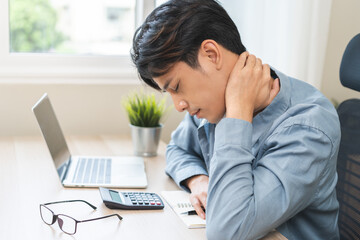 Body muscles stiff problem, ache asian young man pain neck and shoulder while sitting work on chair at home, male holding massaging rubbing, hurt or sore body. Healthcare people, office syndrome.