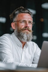 Fototapeta premium Side view portrait of bearded mature male programmer with open laptop in office