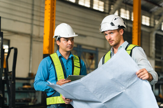 Engineers wearing safety helmets inspecting railway blueprint beside a vintage locomotive, symbolizing teamwork, innovation, and development in modern rail transportation and infrastructure projects