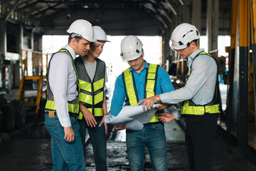 Engineers wearing safety helmets inspecting railway blueprint beside a vintage locomotive, symbolizing teamwork, innovation, and development in modern rail transportation and infrastructure projects