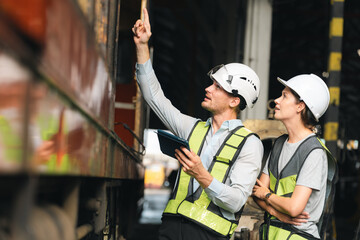 Engineers wearing safety helmets inspecting railway blueprint beside a vintage locomotive,...