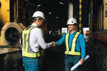 Engineers wearing safety helmets inspecting railway blueprint beside a vintage locomotive, symbolizing teamwork, innovation, and development in modern rail transportation and infrastructure projects