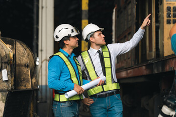 Engineers wearing safety helmets inspecting railway blueprint beside a vintage locomotive, symbolizing teamwork, innovation, and development in modern rail transportation and infrastructure projects