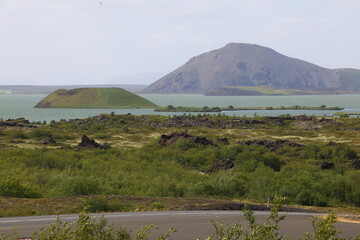 A volcanic crater island rises from the turquoise waters of Lake Mývatn in northern Iceland,...
