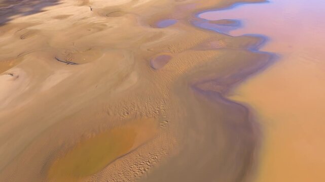 Aerial telephoto view of sandbanks along the Tambopata River with scattered pools, shoreline patterns, and muddy water shaping the Amazon rainforest landscape in Madre de Dios, Peru
