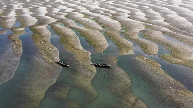 Bogura, Bangladesh - 22 August 2025: Aerial view of two boats resting on the textured sand, showcasing the intricate patterns created by the tide's ebb and flow.