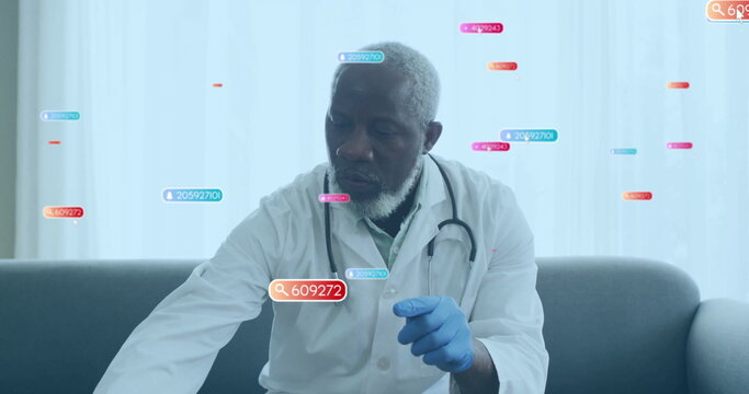 Doctor wearing lab coat, stethoscope and blue gloves viewing data tags on gray sofa under drapes