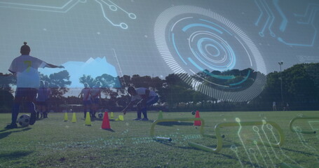 Bending coach placing plastic cone on grass field at park, with soccer ball, jerseys and hurdles