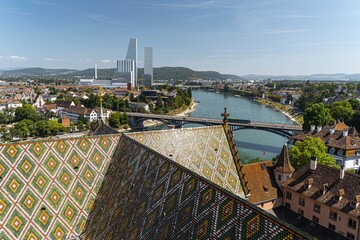 Colourful ornament on the roof of Basel Cathedral with the city panorama and modern skyscrapers in the background.