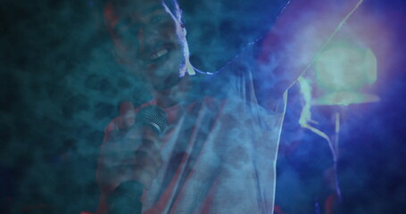 Singing singer wearing plain T-shirt gripping wired microphone on stage, with smoke and spotlight