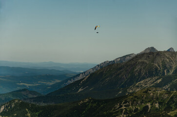Paraglider flying high above the mountains with stunning panoramic views. Adventure and extreme sport.
