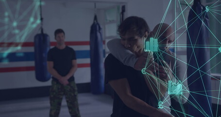 Demonstrating instructor applying hold on student in martial arts dojo with punching bags and mats