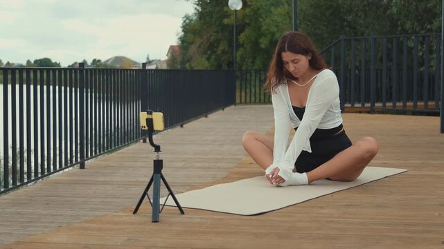 Yoga instructor conducting online fitness class through smartphone while practicing in serene outdoor park setting, embracing wellness and mindful movement