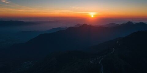 Obraz premium Majestic mountain range shrouded in mist at sunrise with golden sun breaking through clouds