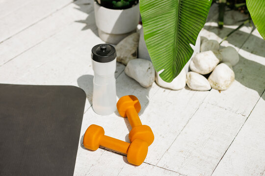 Orange dumbbells and water bottle on outdoor mat with copy space fitness equipment