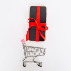Shopping cart with mobile phone with bright red ribbon on white background. selling concept