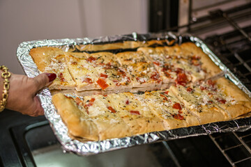 Chef taking out freshly baked garlic bread with cheese and tomatoes from oven
