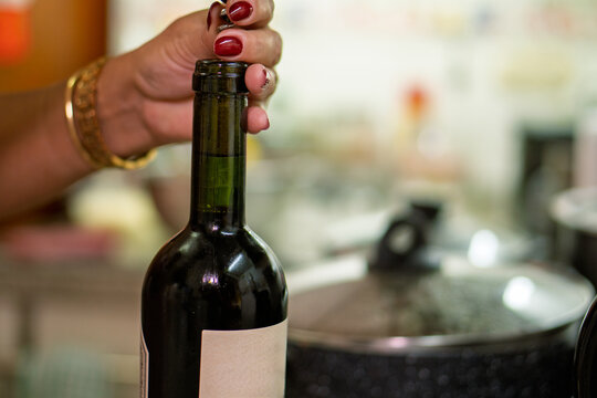 Woman uncorking bottle of red wine in kitchen