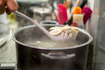 Chef using skimmer to remove cooked ravioli from pot