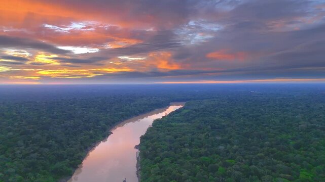 The Tambopata River reflects the vibrant hues of sunset skies as it meanders through dense Amazon rainforest, framed by dramatic clouds on the horizon
