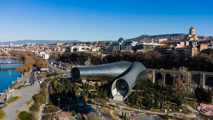 Aerial view showcasing rike park with the modern music hall and exhibition hall near the kura river, alongside the bridge of peace and tbilisi's iconic landmarks under a clear blue sky © wifesun