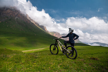 satisfied man stands in a helmet and glasses with a mountain bike under a sky with clouds that...