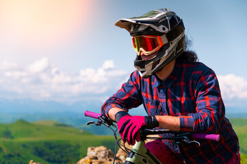 Portrait of a young man in a protective helmet and gloves, in bright clothes, sitting on a downhill...