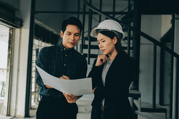 Construction manager and engineer dressed in orange work vests and hard helmets explore...