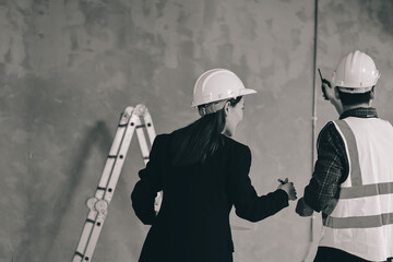 Construction manager and engineer dressed in orange work vests and hard helmets explore...
