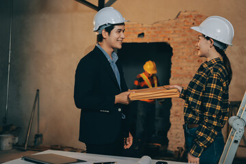 Construction manager and engineer dressed in orange work vests and hard helmets explore...