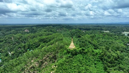 Ramu, Bangladesh - 21 August 2025: Aerial view of a golden pagoda perched atop a lush green hill, contrasting with the distant patchwork of fields.