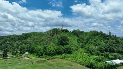 Ramu, Bangladesh - 21 August 2025: Aerial view of a golden pagoda perched atop a lush green hill, contrasting with the bright blue sky and scattered clouds.