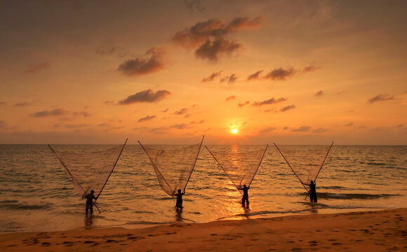 Silhouette of four fishermen standing side by side in the shallows on a beach fishing, Thailand