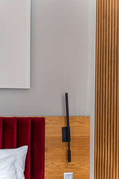 Close-up of a bedroom interior with part of bed, headboard, electric light and blank picture frame hanging on a wall