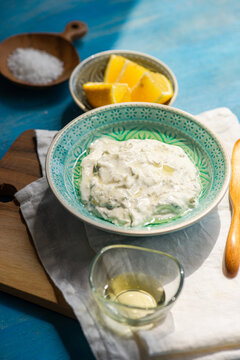 Close-up of a bowl of Traditional tzatziki with sea salt and lemons on a blue wooden table