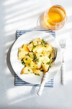 Overhead view of a bowl of traditional Greek potato salad (Patatosalata) on a table with cutlery, napkin and a glass of wine