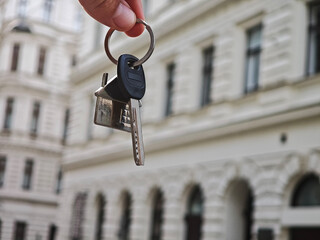 Close-up of hand holding house key and keychain in front of apartment, concept of homeownership