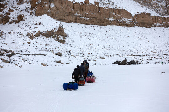 Rear view of a group of Porters hauling supplies over the frozen River Zanskar on the Chadar Trek, Indian Himalayas, Ladakh, India
